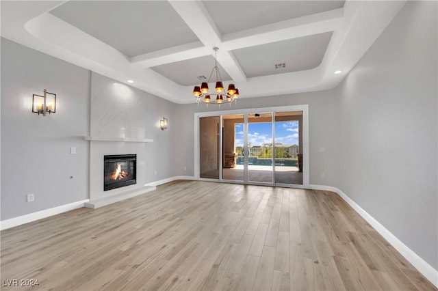 unfurnished living room featuring beam ceiling, a large fireplace, coffered ceiling, an inviting chandelier, and light wood-type flooring