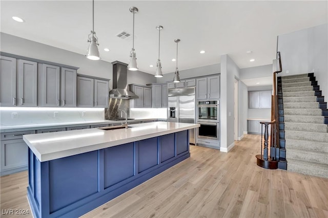 kitchen featuring sink, wall chimney range hood, tasteful backsplash, pendant lighting, and a kitchen island with sink