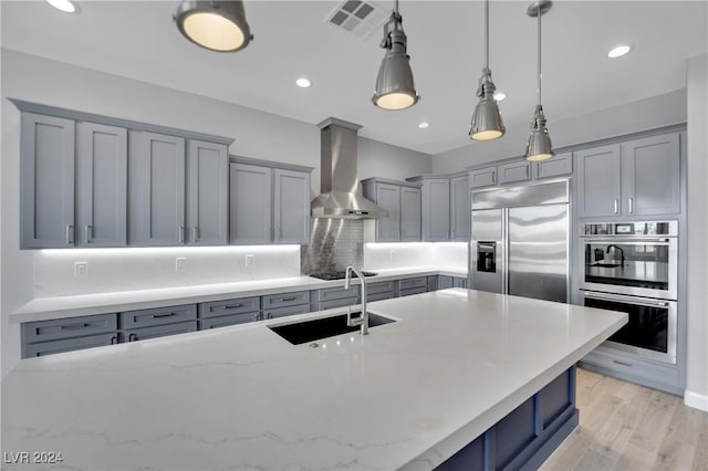 kitchen featuring light stone countertops, appliances with stainless steel finishes, wall chimney exhaust hood, sink, and pendant lighting