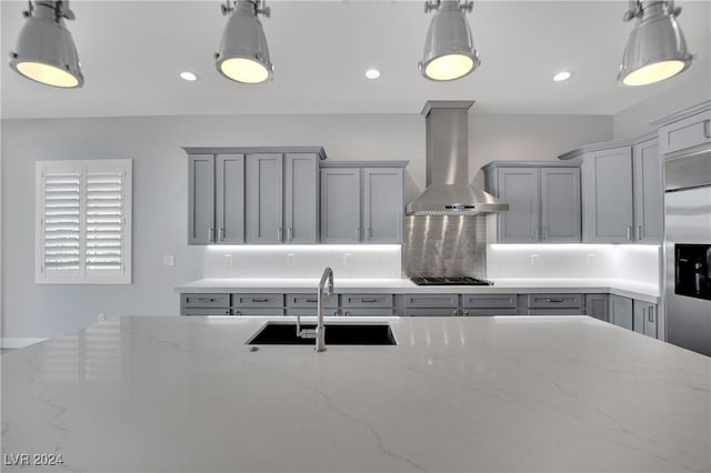 kitchen featuring light stone counters, sink, decorative light fixtures, and wall chimney range hood