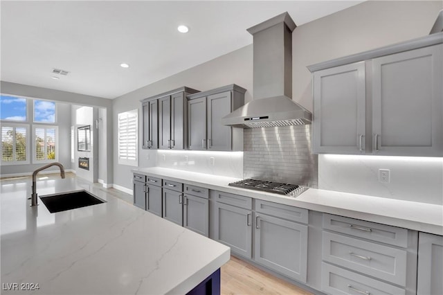 kitchen featuring tasteful backsplash, gray cabinetry, wall chimney exhaust hood, stainless steel gas cooktop, and sink