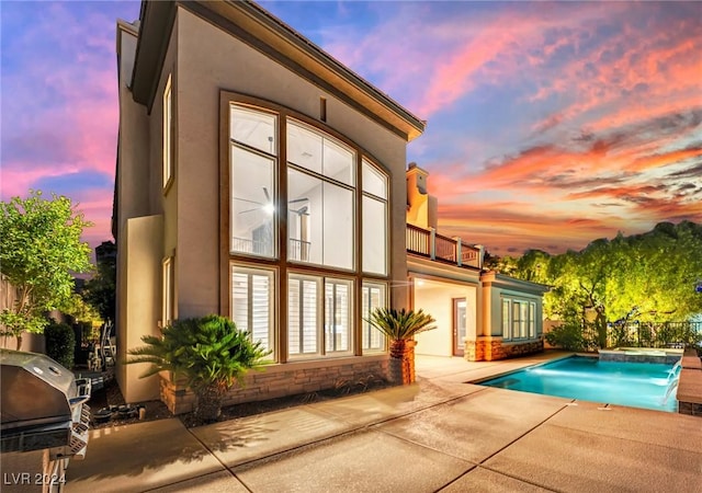 back house at dusk with pool water feature, a balcony, and a patio