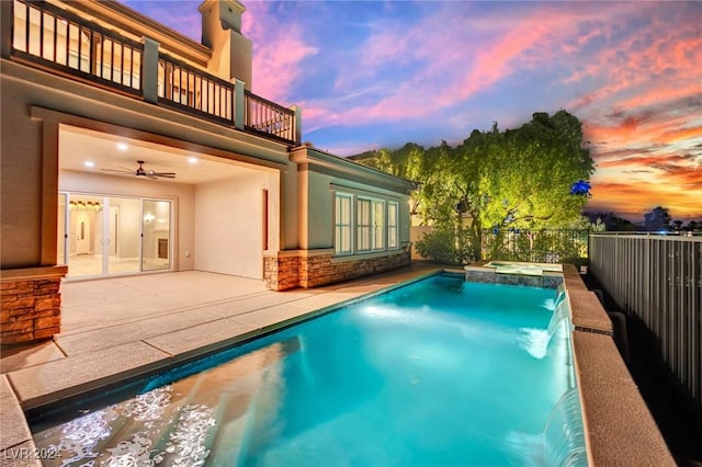 pool at dusk featuring pool water feature, ceiling fan, a patio area, and an in ground hot tub