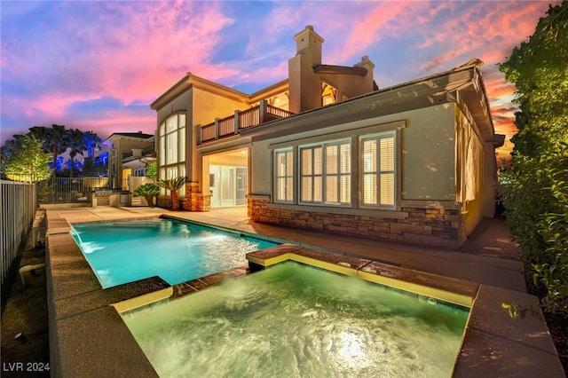 pool at dusk with a patio area, pool water feature, and an in ground hot tub