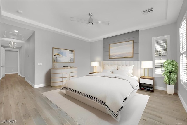 bedroom with light wood-type flooring, a raised ceiling, and ceiling fan