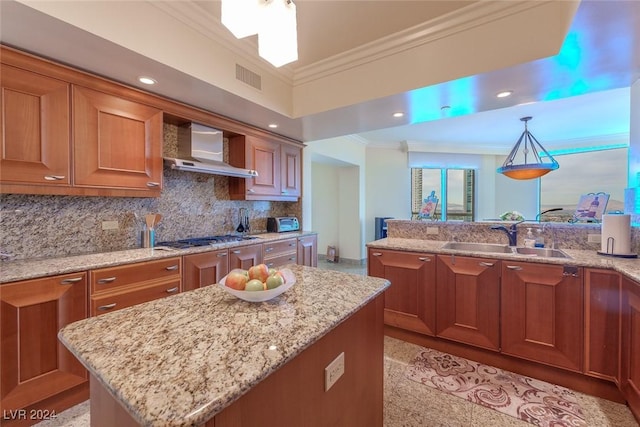 kitchen featuring wall chimney range hood, sink, light stone countertops, decorative light fixtures, and a kitchen island