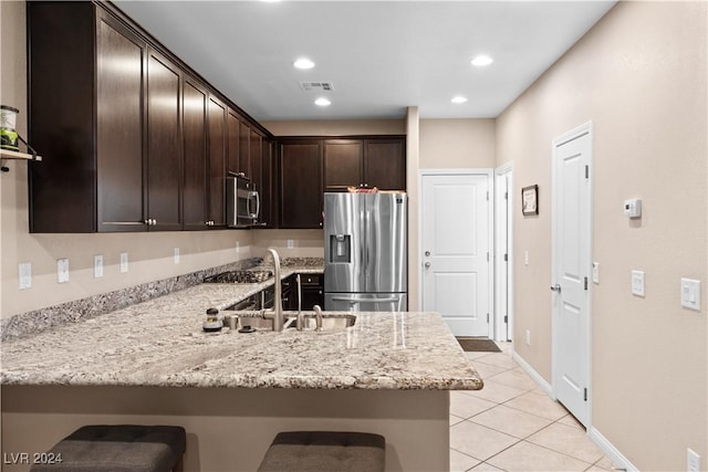 kitchen with sink, stainless steel appliances, light stone counters, dark brown cabinets, and light tile patterned flooring