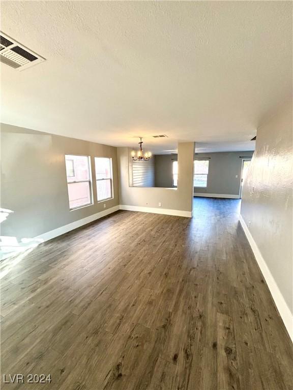 unfurnished living room with a textured ceiling, an inviting chandelier, and dark hardwood / wood-style flooring