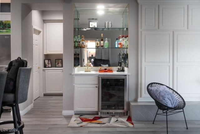 bar featuring white cabinets, sink, beverage cooler, and light wood-type flooring