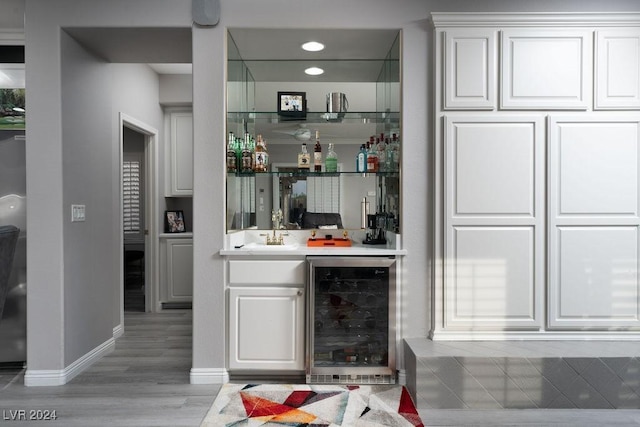 bar featuring white cabinetry, beverage cooler, sink, and light hardwood / wood-style flooring