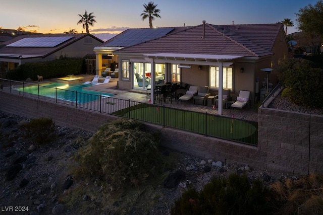 back house at dusk with outdoor lounge area, a fenced in pool, a patio area, and solar panels