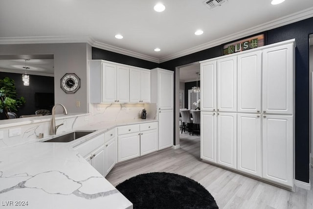 kitchen with pendant lighting, white cabinetry, sink, ornamental molding, and light stone counters