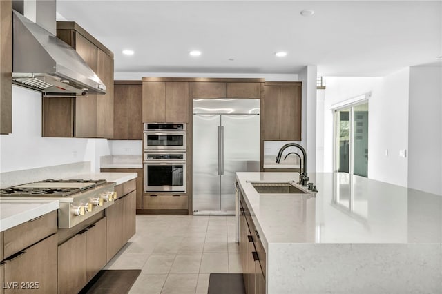 kitchen featuring wall chimney range hood, light tile patterned floors, sink, appliances with stainless steel finishes, and a spacious island