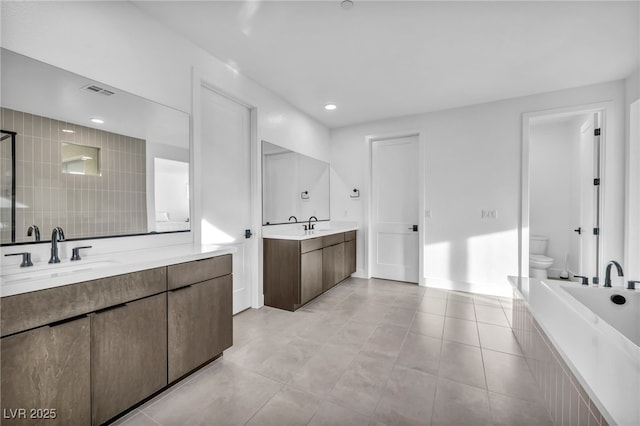 bathroom featuring vanity, a relaxing tiled tub, tile patterned floors, and toilet