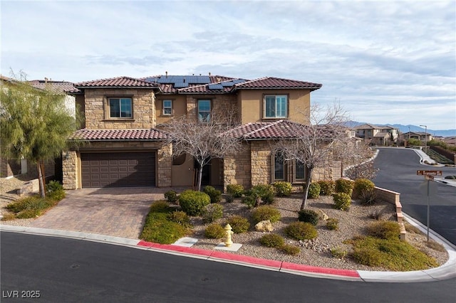 mediterranean / spanish home with decorative driveway, stone siding, a tile roof, and solar panels