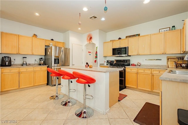 kitchen featuring a center island, light tile patterned floors, light brown cabinets, and appliances with stainless steel finishes