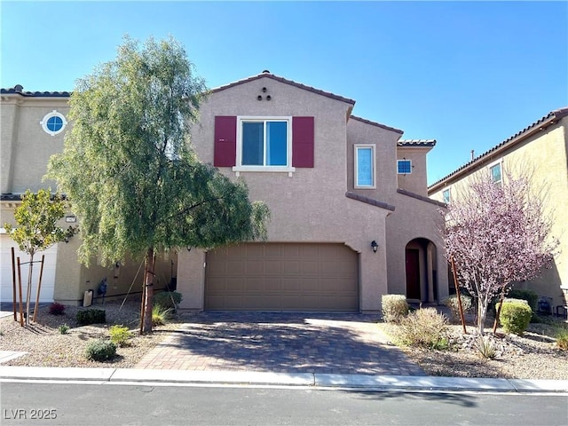 mediterranean / spanish house with a garage, a tiled roof, decorative driveway, and stucco siding