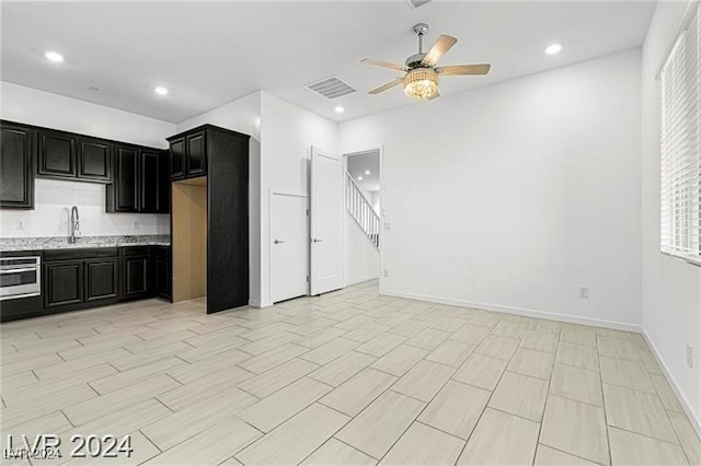 kitchen featuring oven, ceiling fan, light stone counters, and sink