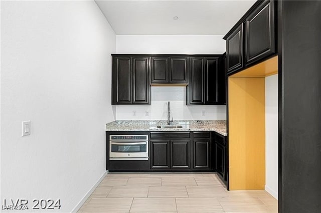 kitchen featuring light stone counters, stainless steel oven, and sink