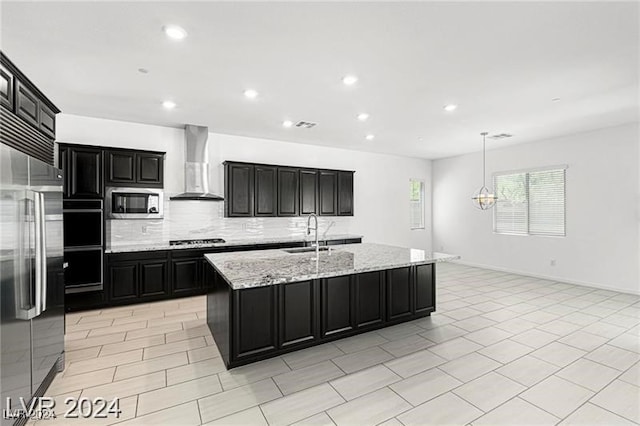 kitchen featuring a kitchen island with sink, hanging light fixtures, sink, wall chimney exhaust hood, and stainless steel appliances