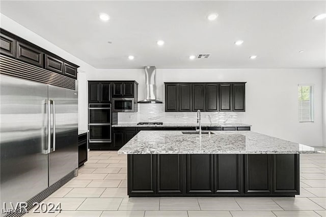 kitchen with a kitchen island with sink, sink, wall chimney exhaust hood, appliances with stainless steel finishes, and tasteful backsplash