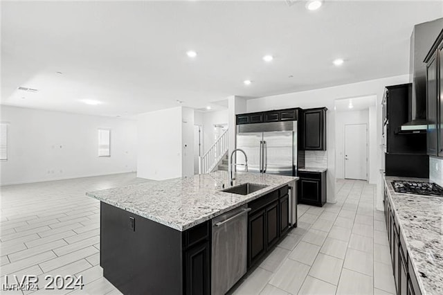 kitchen featuring sink, light stone countertops, an island with sink, and stainless steel appliances