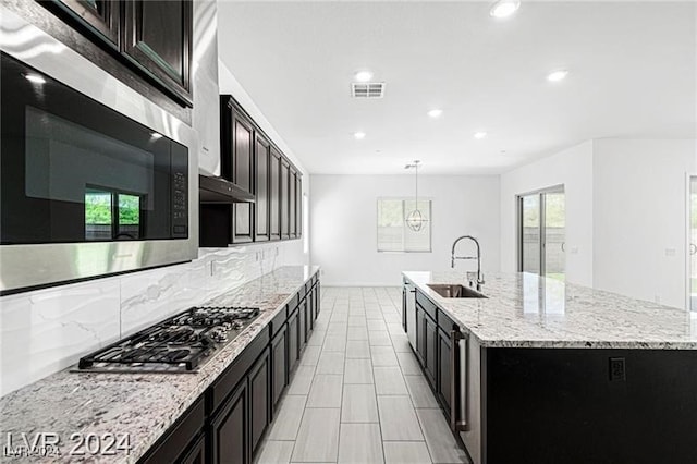 kitchen featuring decorative backsplash, appliances with stainless steel finishes, sink, a center island with sink, and hanging light fixtures