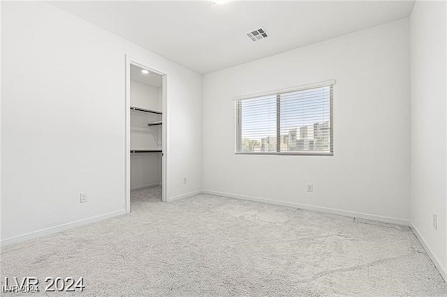 unfurnished bedroom featuring a walk in closet, light carpet, and a closet