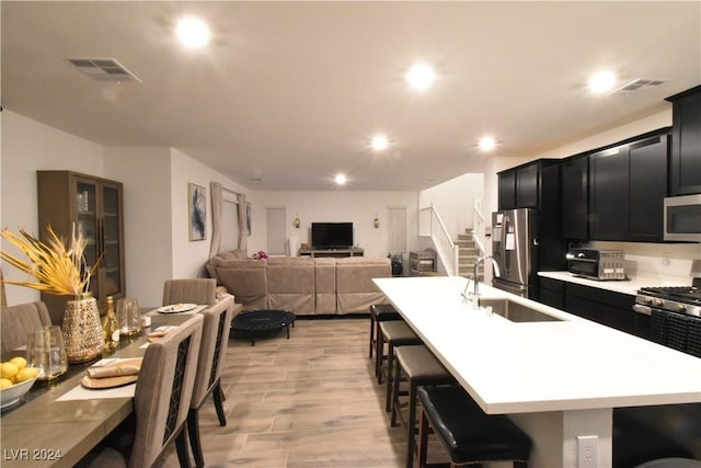 kitchen featuring a kitchen breakfast bar, stainless steel appliances, a kitchen island with sink, sink, and light hardwood / wood-style floors