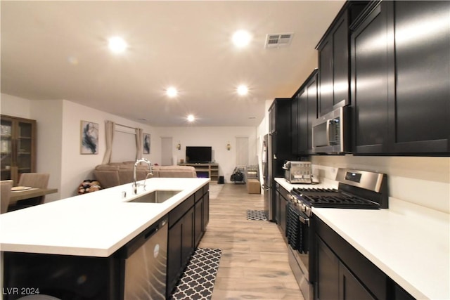 kitchen with light hardwood / wood-style flooring, sink, appliances with stainless steel finishes, and an island with sink