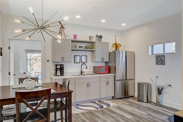 kitchen featuring pendant lighting, sink, light hardwood / wood-style flooring, stainless steel fridge, and a notable chandelier