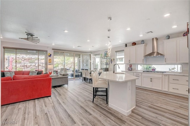 kitchen with a center island with sink, white cabinets, sink, wall chimney exhaust hood, and light hardwood / wood-style floors