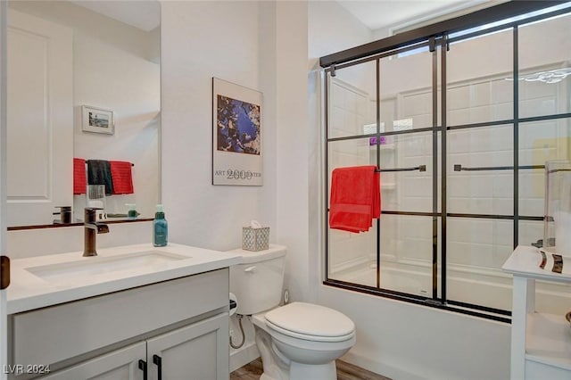 full bathroom with shower / bath combination with glass door, vanity, hardwood / wood-style flooring, and toilet