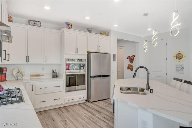 kitchen with stainless steel appliances, sink, a center island with sink, white cabinets, and hanging light fixtures