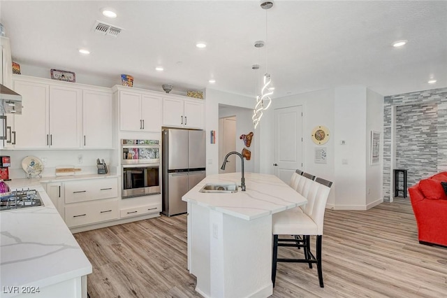 kitchen with stainless steel appliances, sink, pendant lighting, white cabinetry, and an island with sink