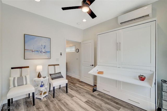 sitting room with ceiling fan, an AC wall unit, and light hardwood / wood-style flooring