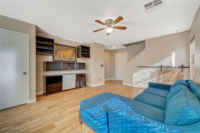 living room with a barn door, light hardwood / wood-style flooring, and ceiling fan