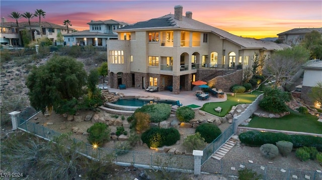 back house at dusk featuring a balcony and a patio