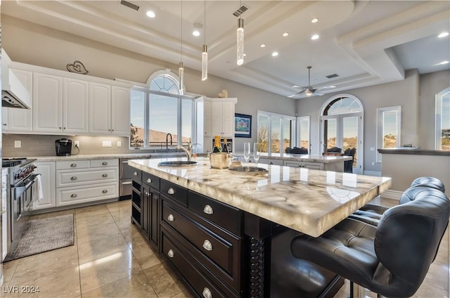 kitchen with a tray ceiling, a kitchen island with sink, white cabinetry, and a breakfast bar area