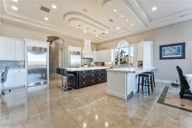 kitchen featuring built in fridge, a kitchen island, a raised ceiling, and premium range hood