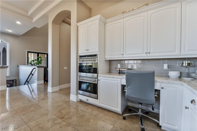 kitchen with double oven, light stone counters, white cabinets, and backsplash