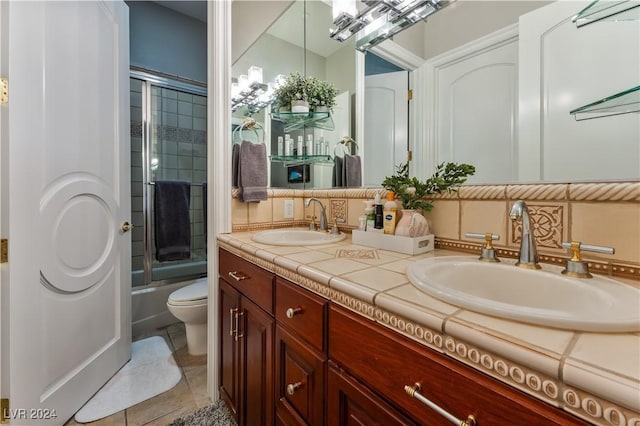 full bathroom with combined bath / shower with glass door, backsplash, vanity, tile patterned flooring, and toilet