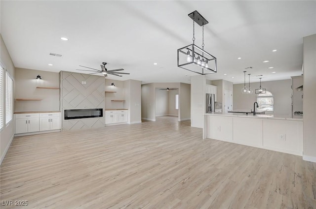 unfurnished living room with a large fireplace, ceiling fan, sink, and light wood-type flooring