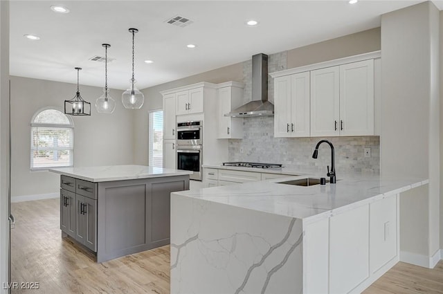 kitchen featuring sink, wall chimney exhaust hood, a kitchen island, tasteful backsplash, and white cabinets