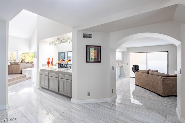 corridor featuring lofted ceiling, visible vents, a sink, and baseboards