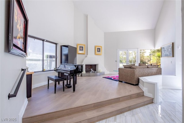 living room with high vaulted ceiling, a fireplace with raised hearth, baseboards, and wood finished floors