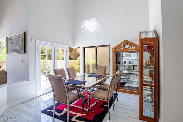 dining space featuring marble finish floor, baseboards, a high ceiling, and an inviting chandelier