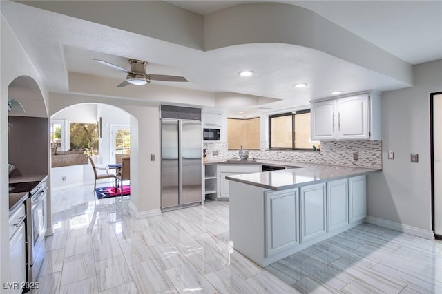 kitchen featuring built in appliances, a peninsula, light countertops, decorative backsplash, and a tray ceiling