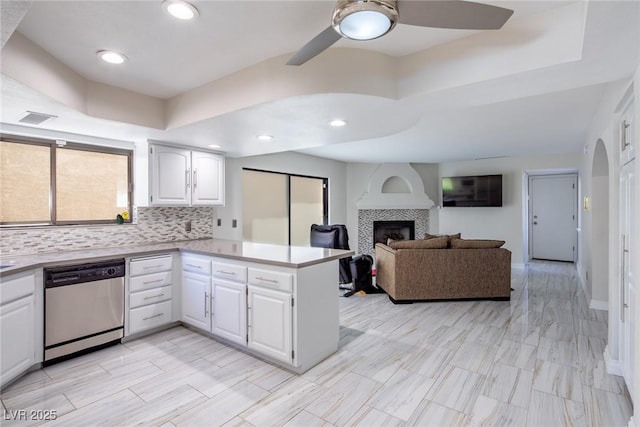 kitchen with arched walkways, a raised ceiling, dishwasher, a peninsula, and a fireplace