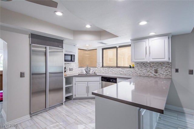 kitchen with tasteful backsplash, appliances with stainless steel finishes, white cabinets, a sink, and a peninsula